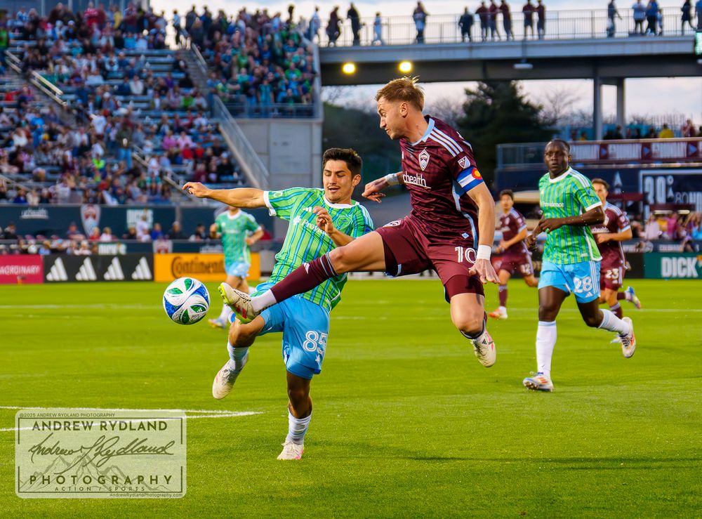 Soccer players from opposing teams leap for ball during intense match action.