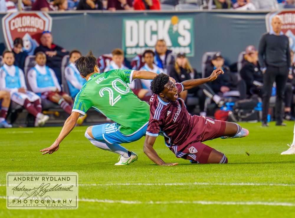 Two players collide and fall during competitive soccer match action.
