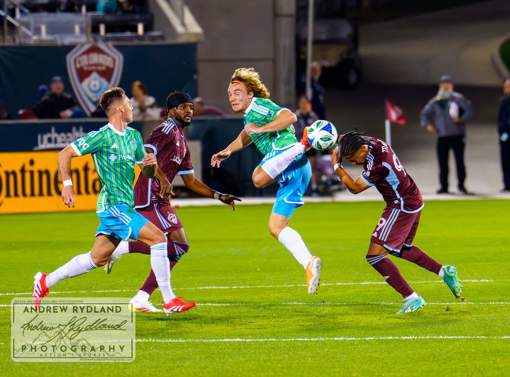 Athletic soccer player jumps high to control ball between two defenders.