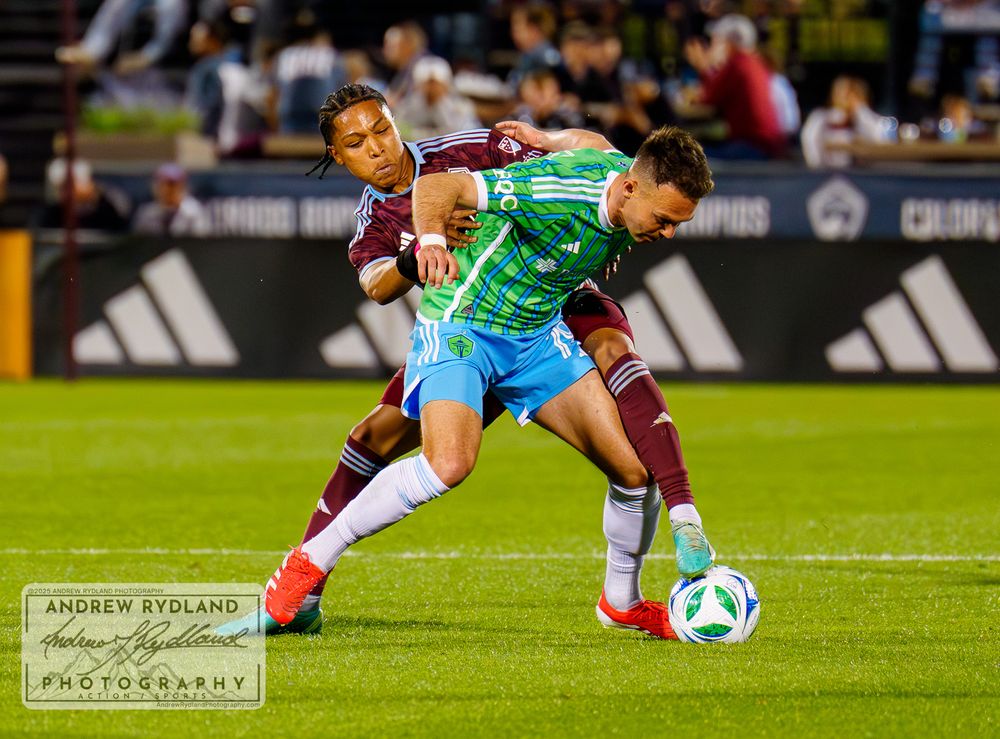 Soccer player in green jersey shields ball from defender during match.