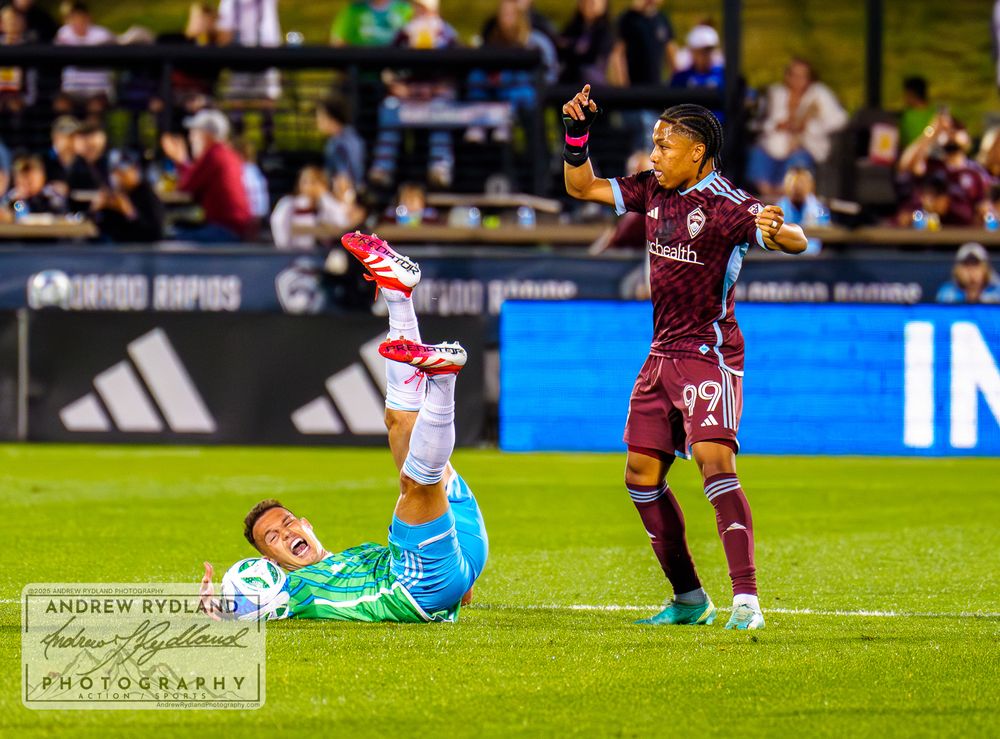 Soccer player on ground as opponent gestures during competitive match.