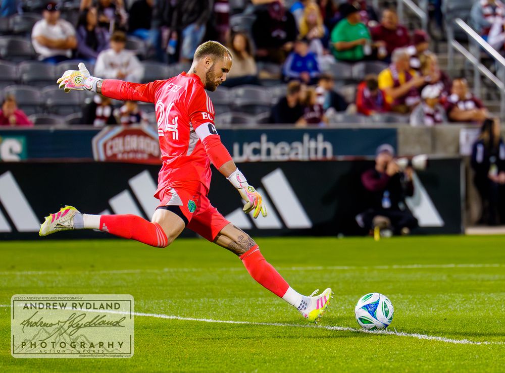 Goalkeeper in red uniform prepares to kick ball during soccer match.