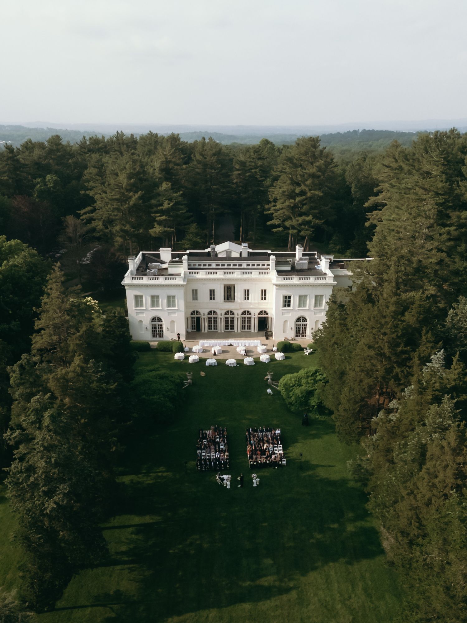 Aerial view of a grand white mansion estate surrounded by lush green trees.