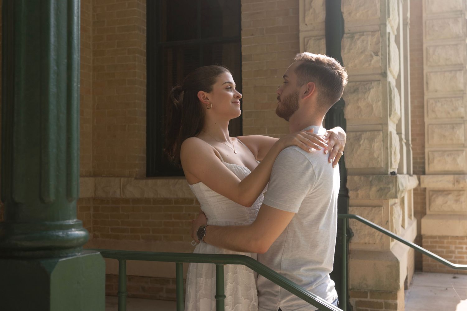Couple dances in romantic embrace near sunlit architectural columns.