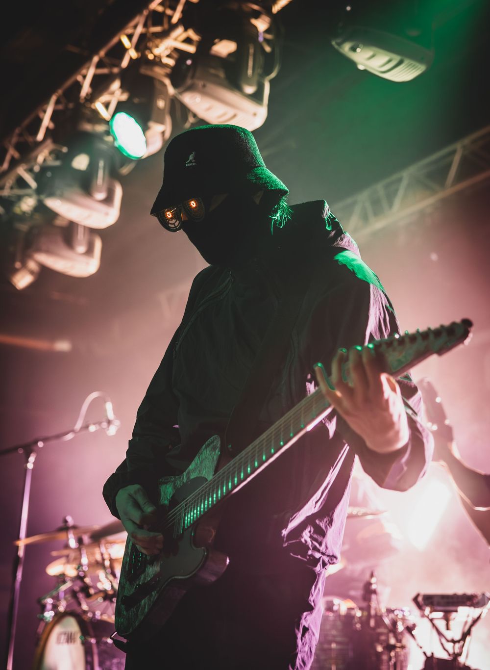 Silhouetted musician performs on stage with dramatic green and purple lighting effects during a live concert performance.