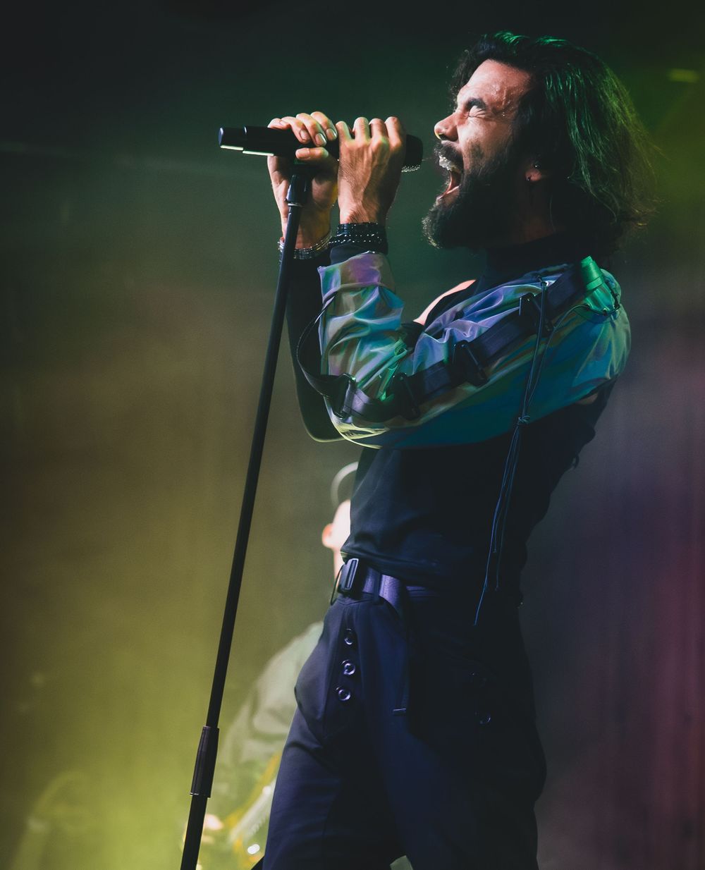 A performer singing passionately on stage under dramatic green and blue lighting during a concert performance.