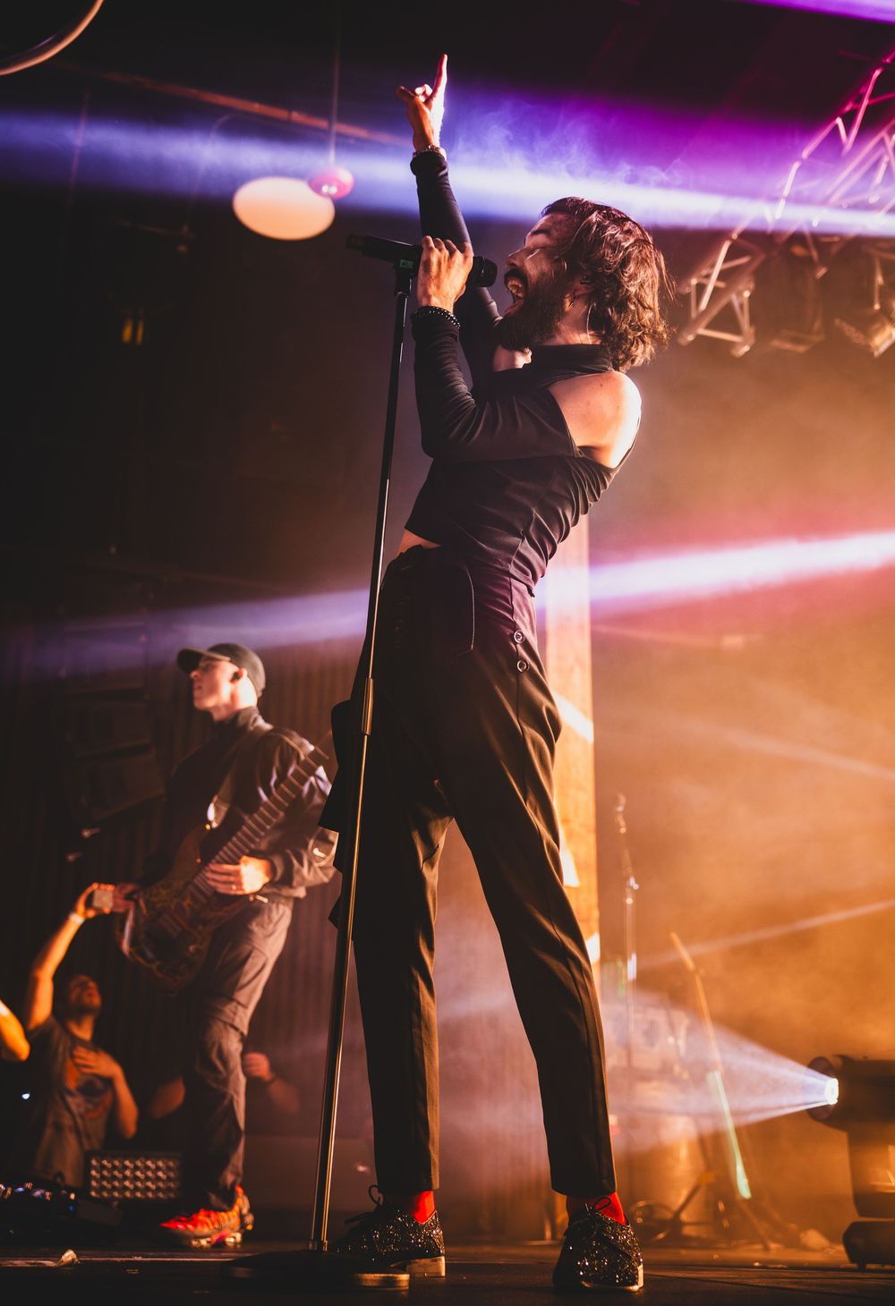 A musician performs passionately on stage with purple and orange lighting effects during a concert performance.