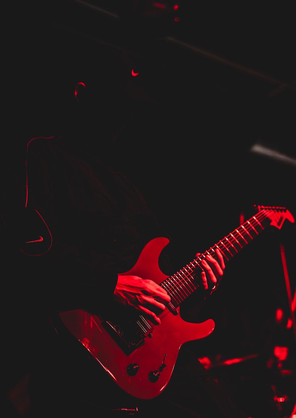Red electric guitar being played on dark stage with dramatic lighting effects.