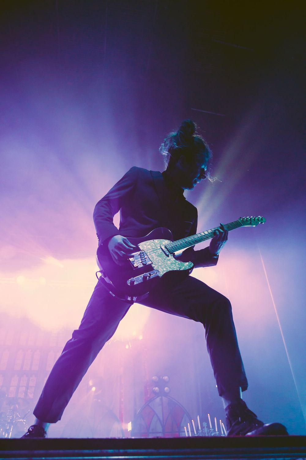 Silhouetted guitarist performs on stage with dramatic purple and blue lighting effects during a live concert performance.