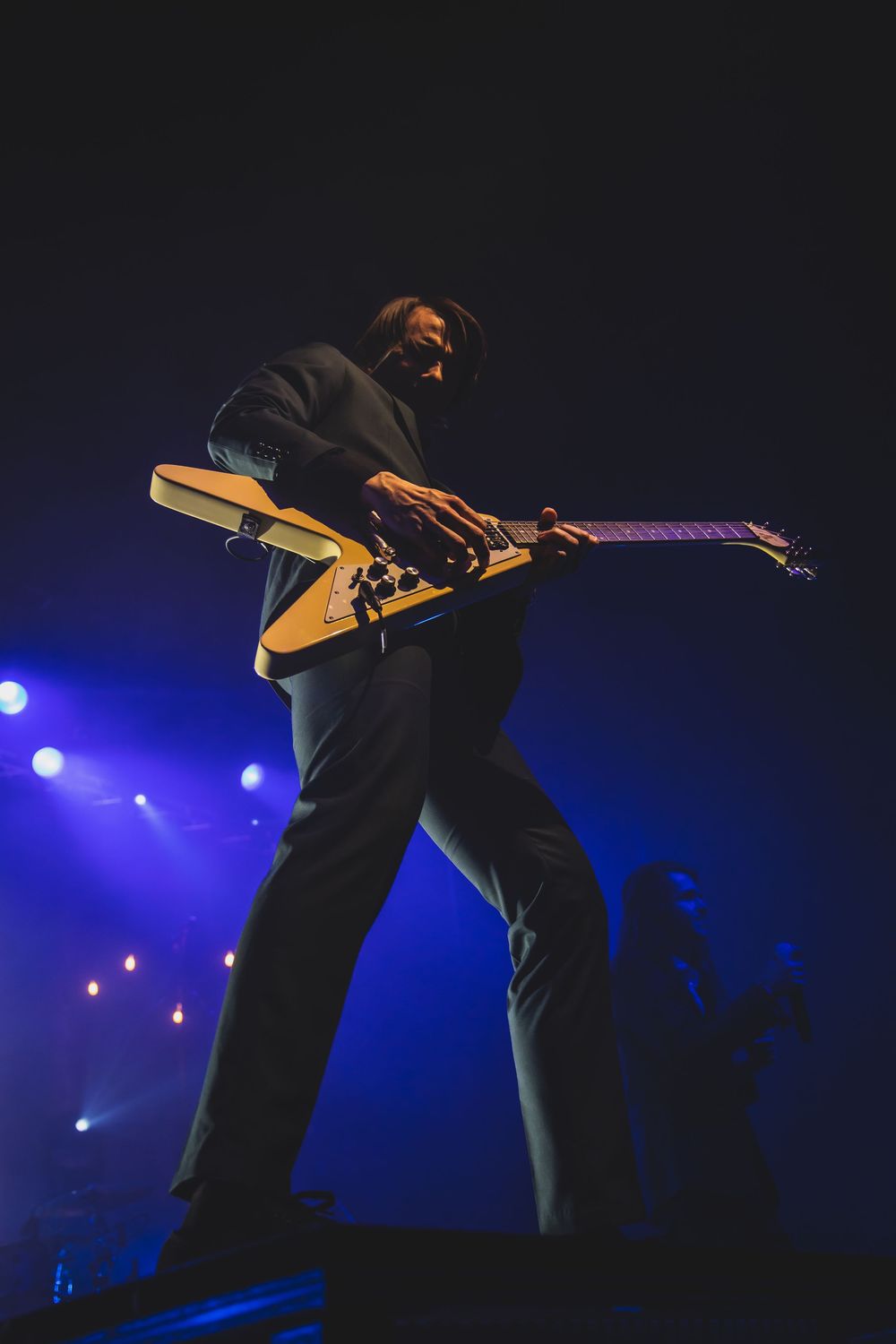 A musician performs on stage with a guitar silhouetted against blue concert lighting and fog.