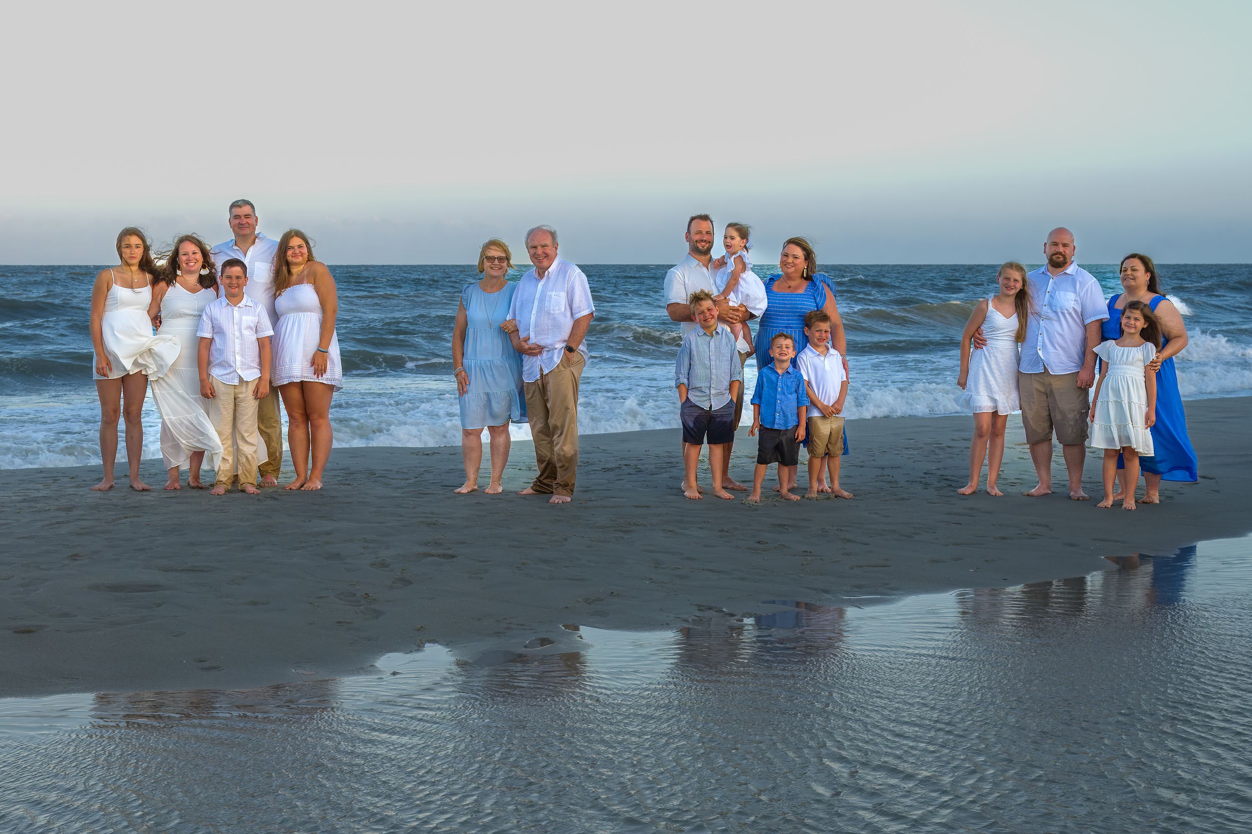 Group of people in coordinated blue and white outfits posing together on a beach at sunset.