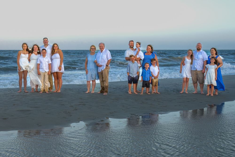 Group of people in coordinated blue and white outfits posing together on a beach at sunset.