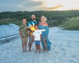A group on a beach at sunset holding surfboards and posing together against coastal dunes in the background.