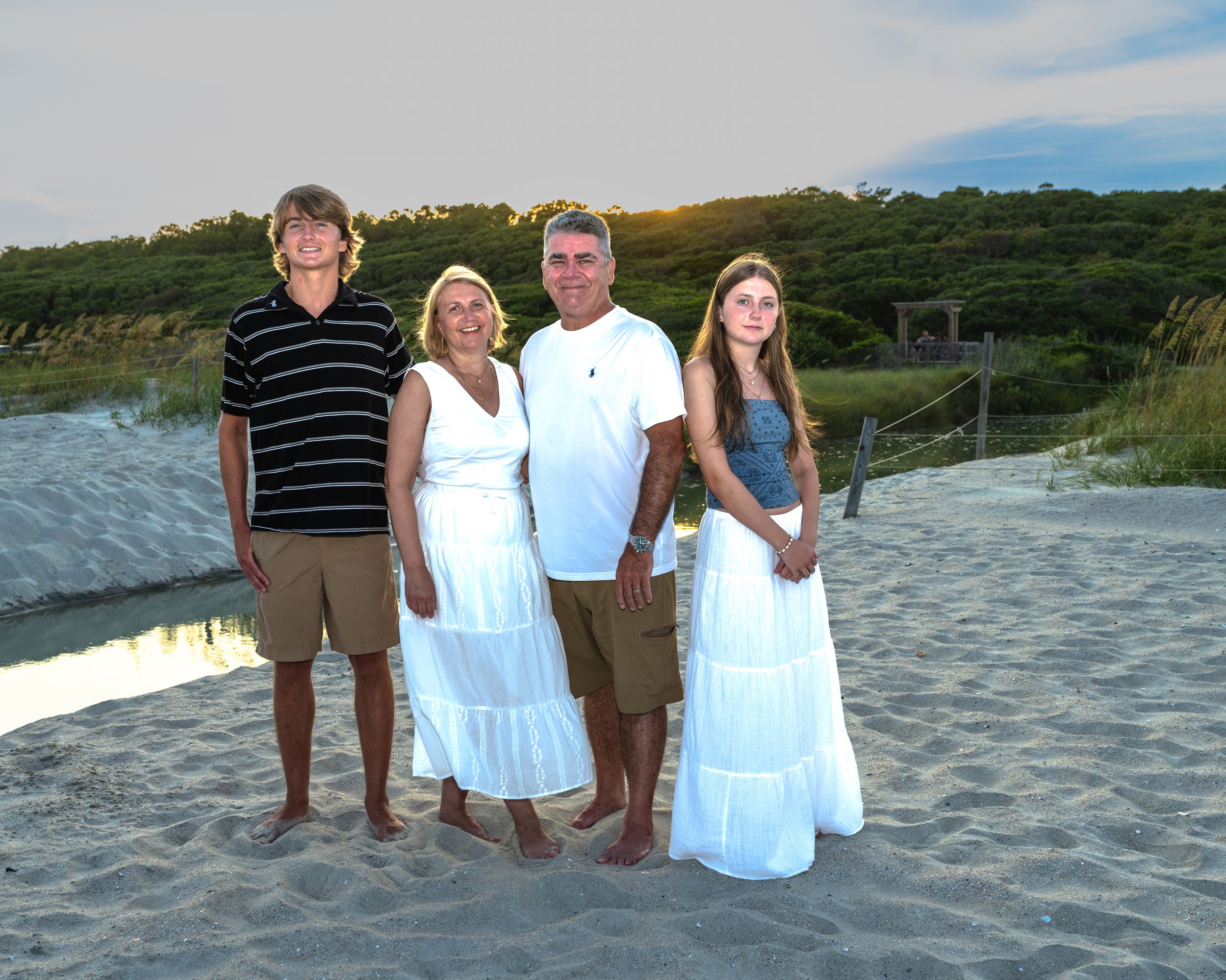 People in white outfits standing together on a beach during sunset with ocean waves visible in the background.