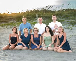 A group of people in casual beachwear sitting together on sand dunes at sunset.