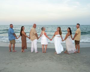 A group of people holding hands while standing on a beach at sunset with ocean waves in the background.