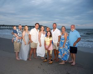 A group of people pose together on a beach at sunset with an ocean pier visible in the background.
