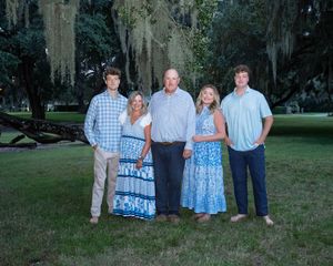 A group wearing coordinated blue and white outfits poses together in a park setting with Spanish moss hanging from trees.