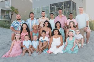 A group in coordinated pastel outfits poses together on a beach during sunset.