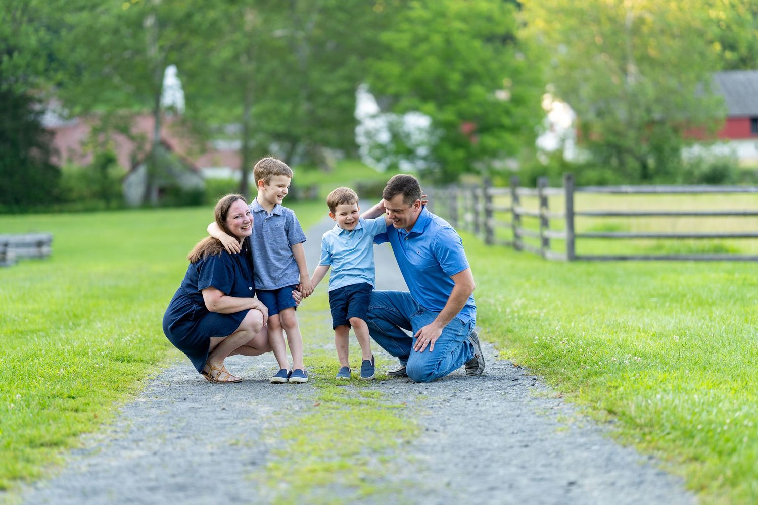 Family spending time together exploring and laughing together on a gravel path surrounded by green grass and wooden fences.
