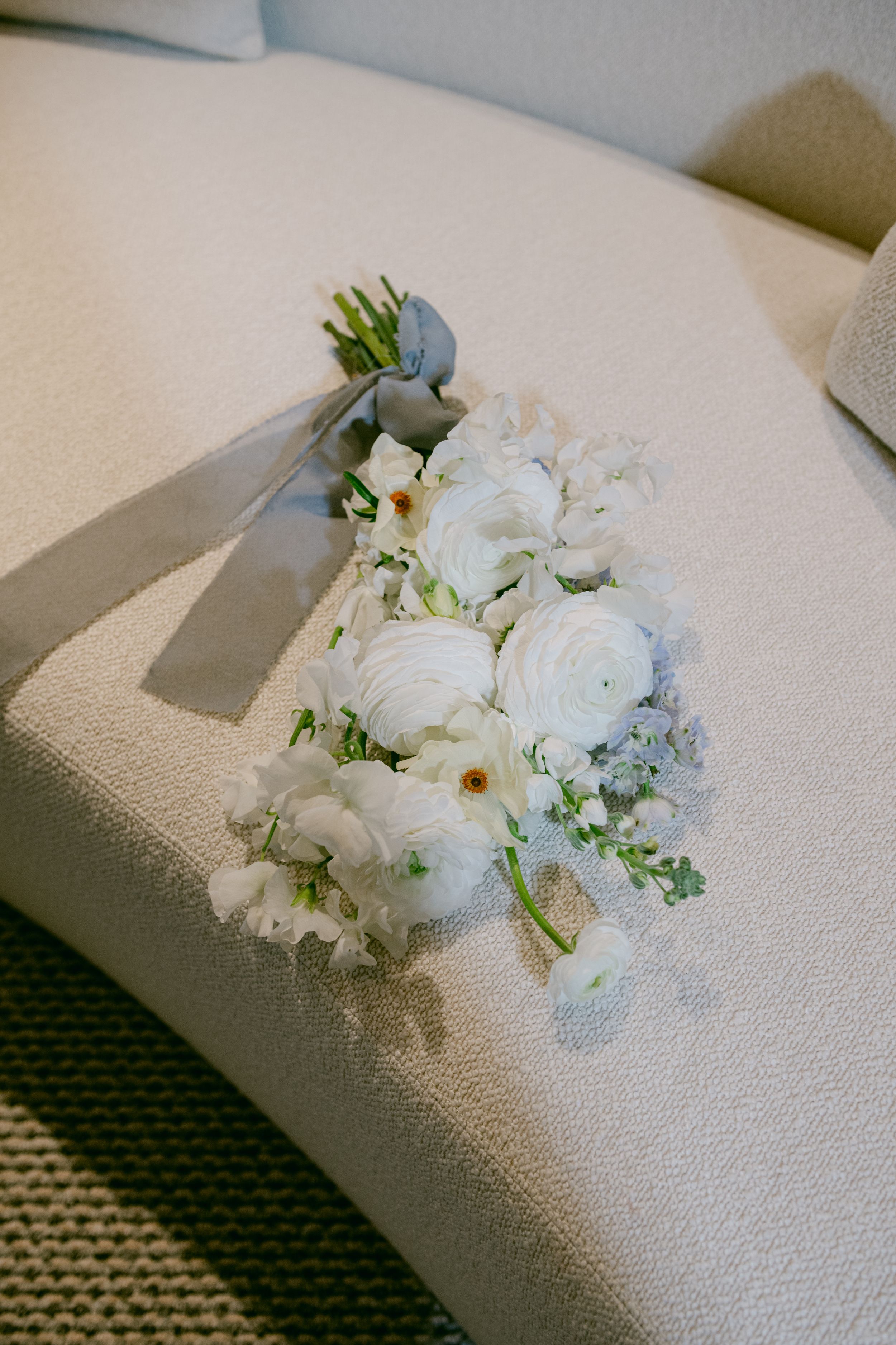 A delicate white floral bouquet with roses and small blossoms rests on a cream-colored fabric.