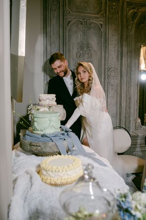 A wedding couple cuts their multi-tiered cake together in an elegant room with ornate wall details.
