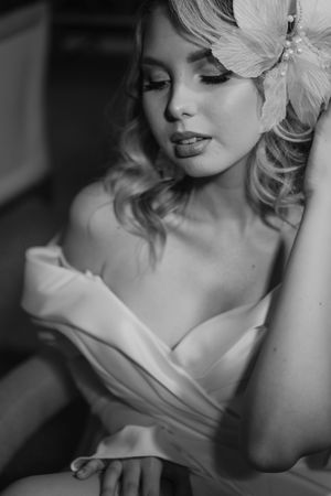 Black and white portrait of an elegant woman in a wrapped white dress with wavy hair and a feather accessory.