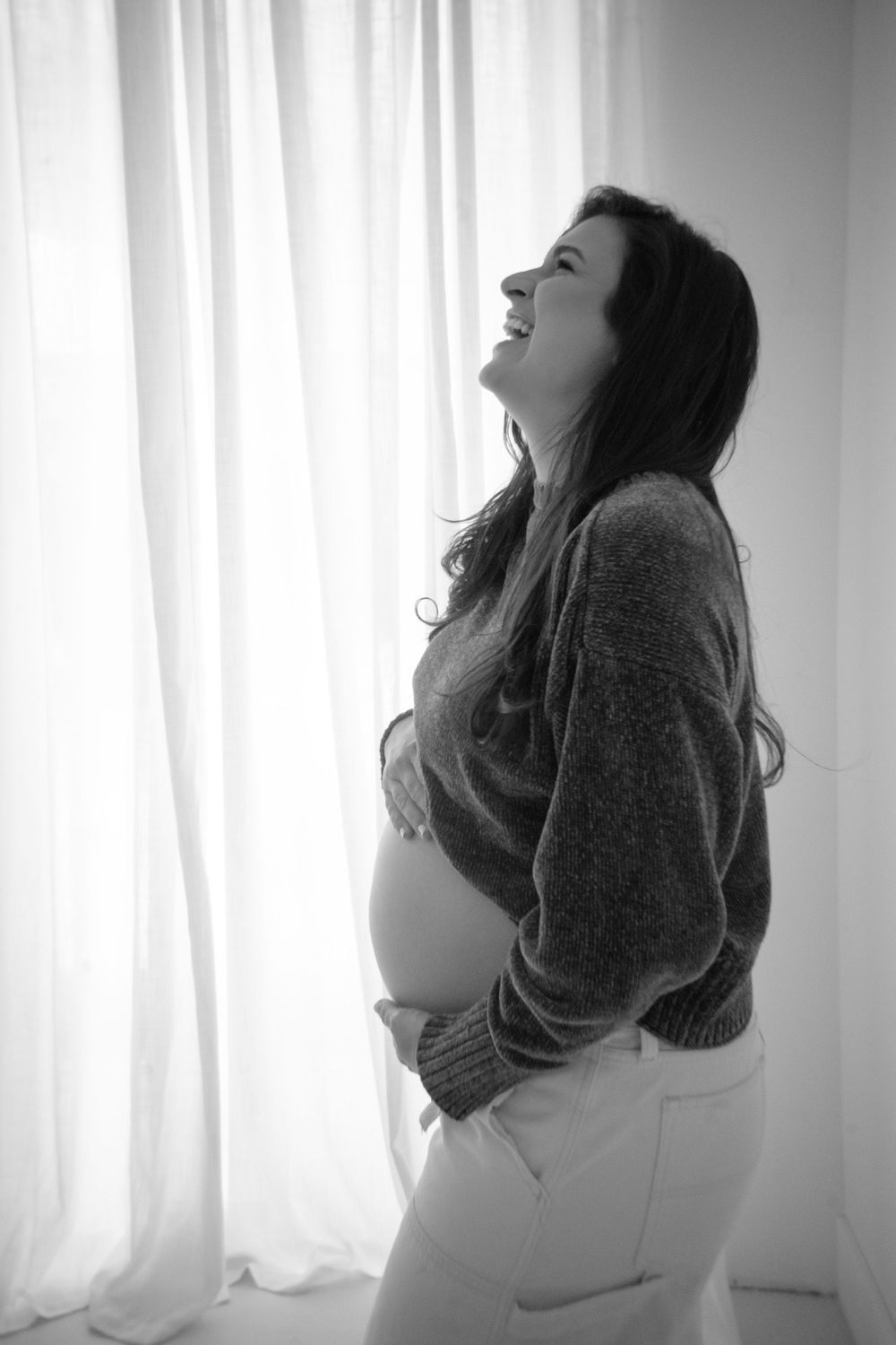 Black and white maternity portrait series showing joyful expressions near window light.