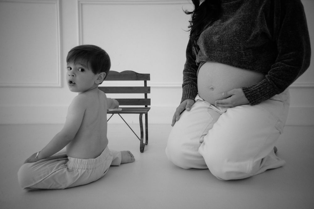 Black and white side profile of pregnant mother and child sitting together on floor during photo session.