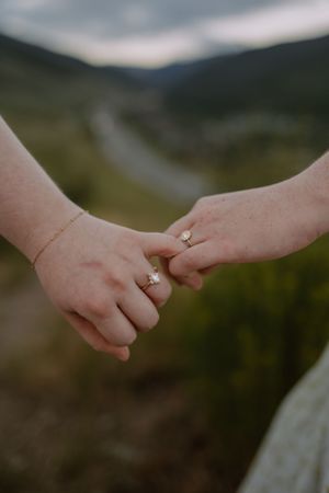 Closeup of brides' hands, holding each other's pinky fingers and showing off their engagement rings.