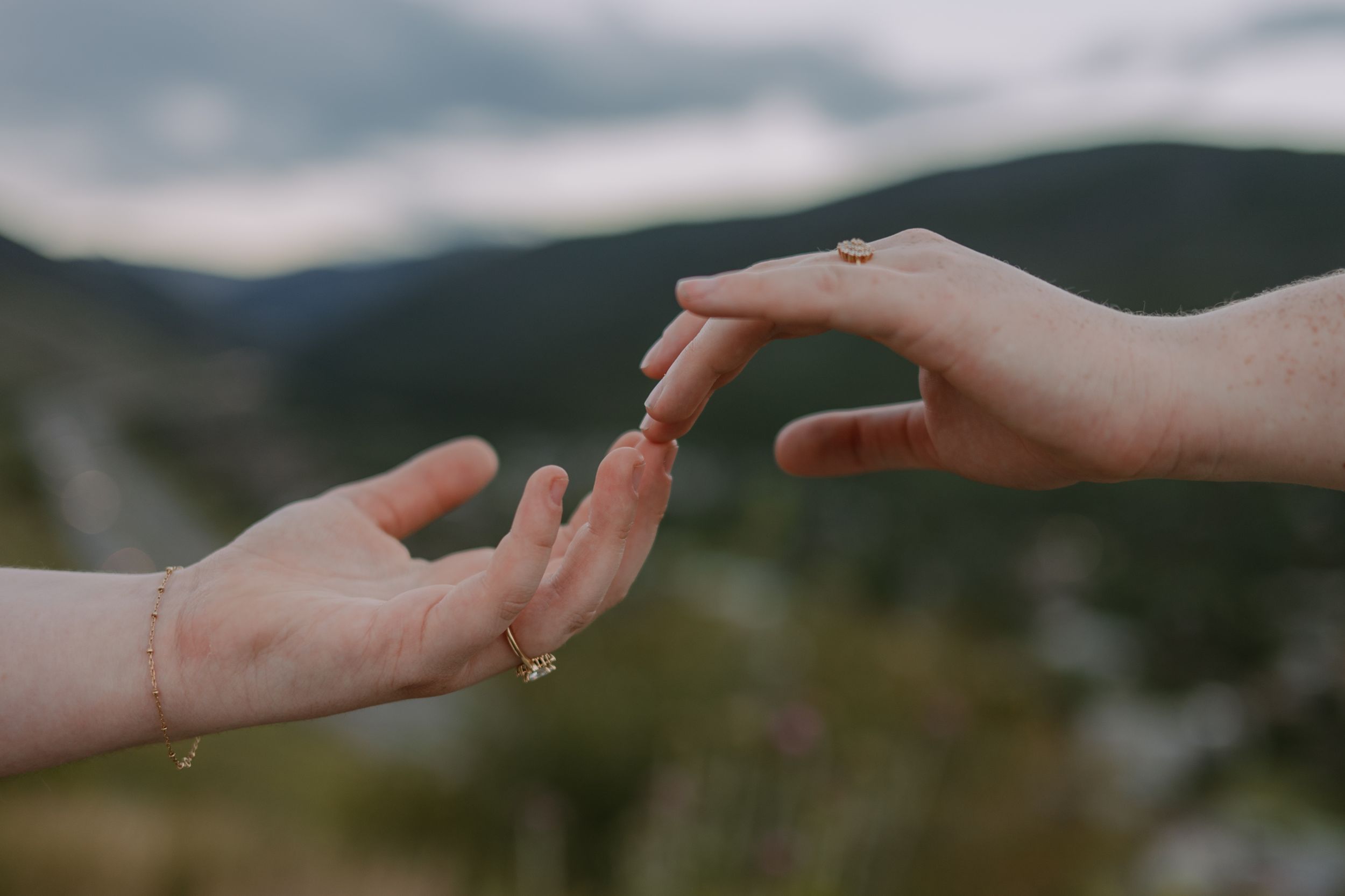 Closeup of Emma and Victoria's hands, fingertips barely touching, mountains blurred in the background