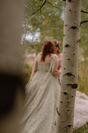 LGBTQ+ couple Victoria and Emma embrace, the camera peeking through the aspen trees to see them.