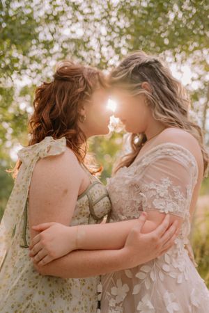 Closeup of Emma and Victoria standing face to face and embracing, the sun peeking through and obscuring their eyes.