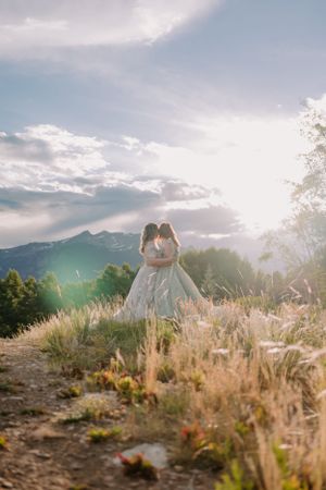 Wide shot of LGBTQ+ white brides standing face to face and kissing on a mountain trail in Colorado.
