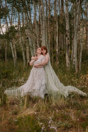 Emma and Victoria embrace in front of aspen trees on a trail in Colorado.