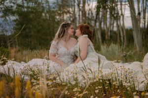 LGBTQ+ brides Emma and Victoria sit among the wildflowers, their wedding dresses splayed out next to them.
