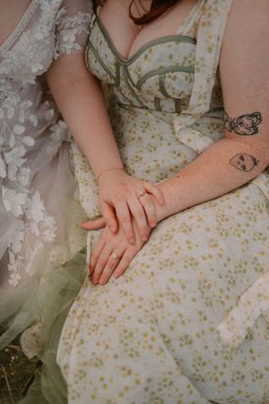 Closeup of brides' hands wearing their engagement rings, hands folded together on Emma's lap while sitting in the grass.