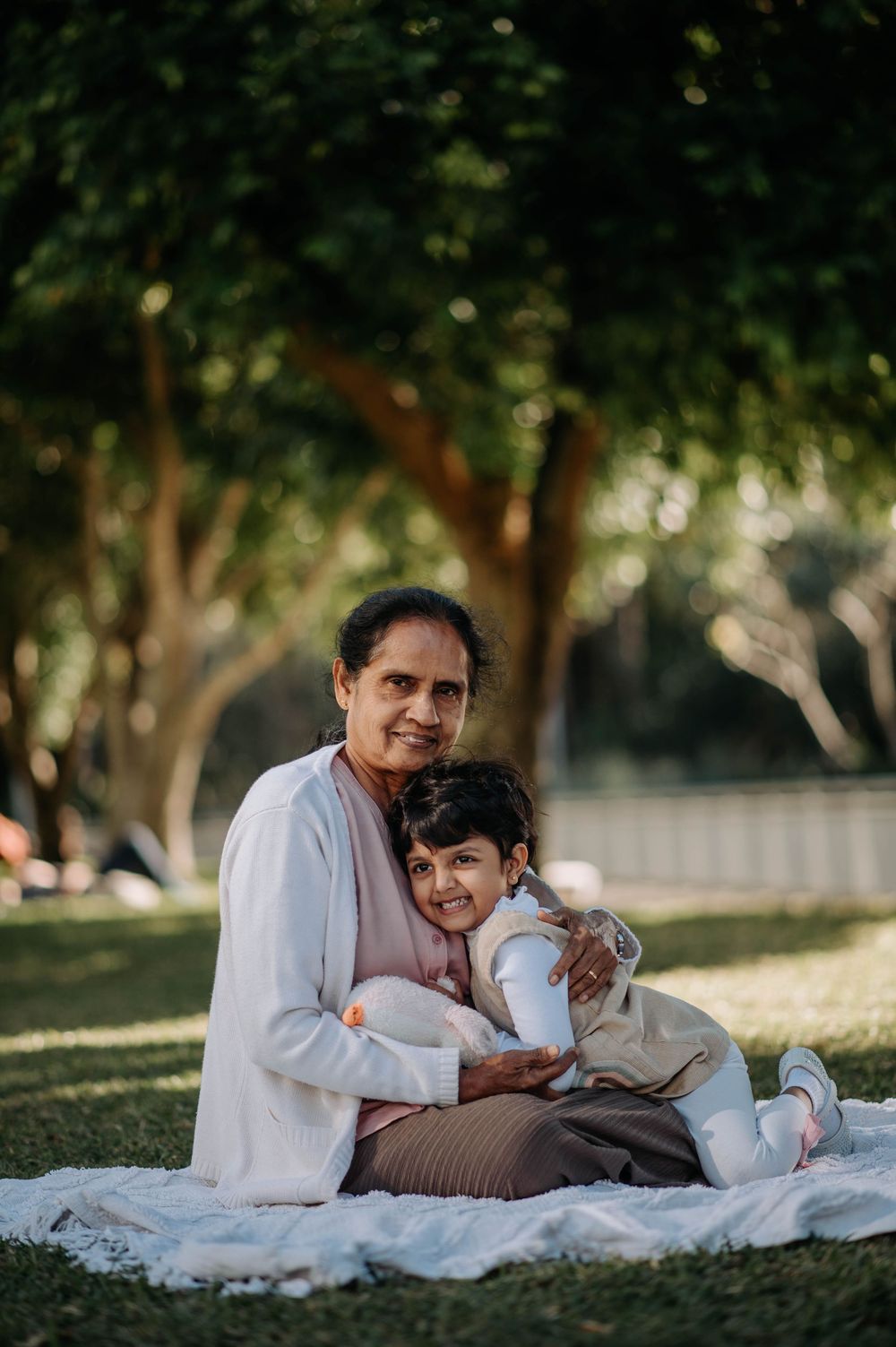 Family enjoying tender moment together on picnic blanket outdoors in a tranquil garden setting during sunset.