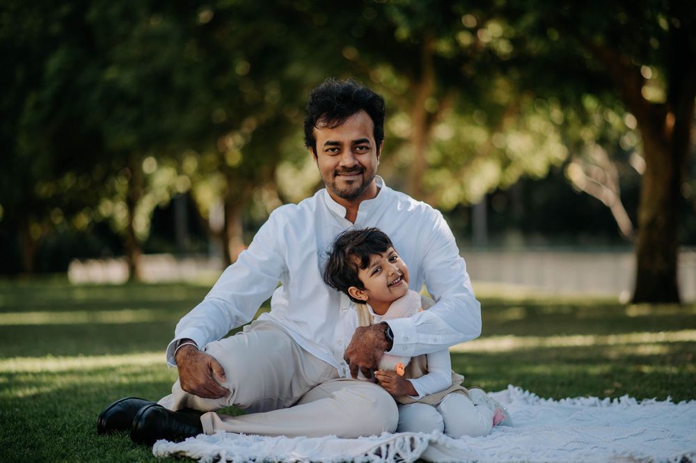 A family in white outfits lay together on green grass during a sunny outdoor photo session.