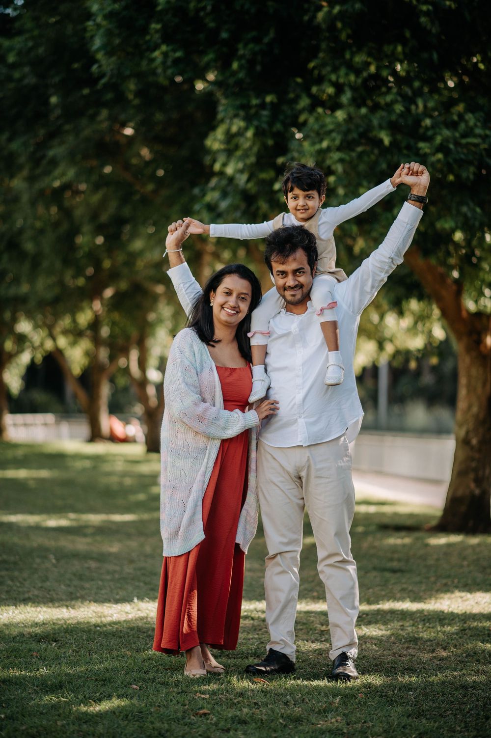 A family enjoying a sunny day together outdoors with a child riding on shoulders in a park setting.