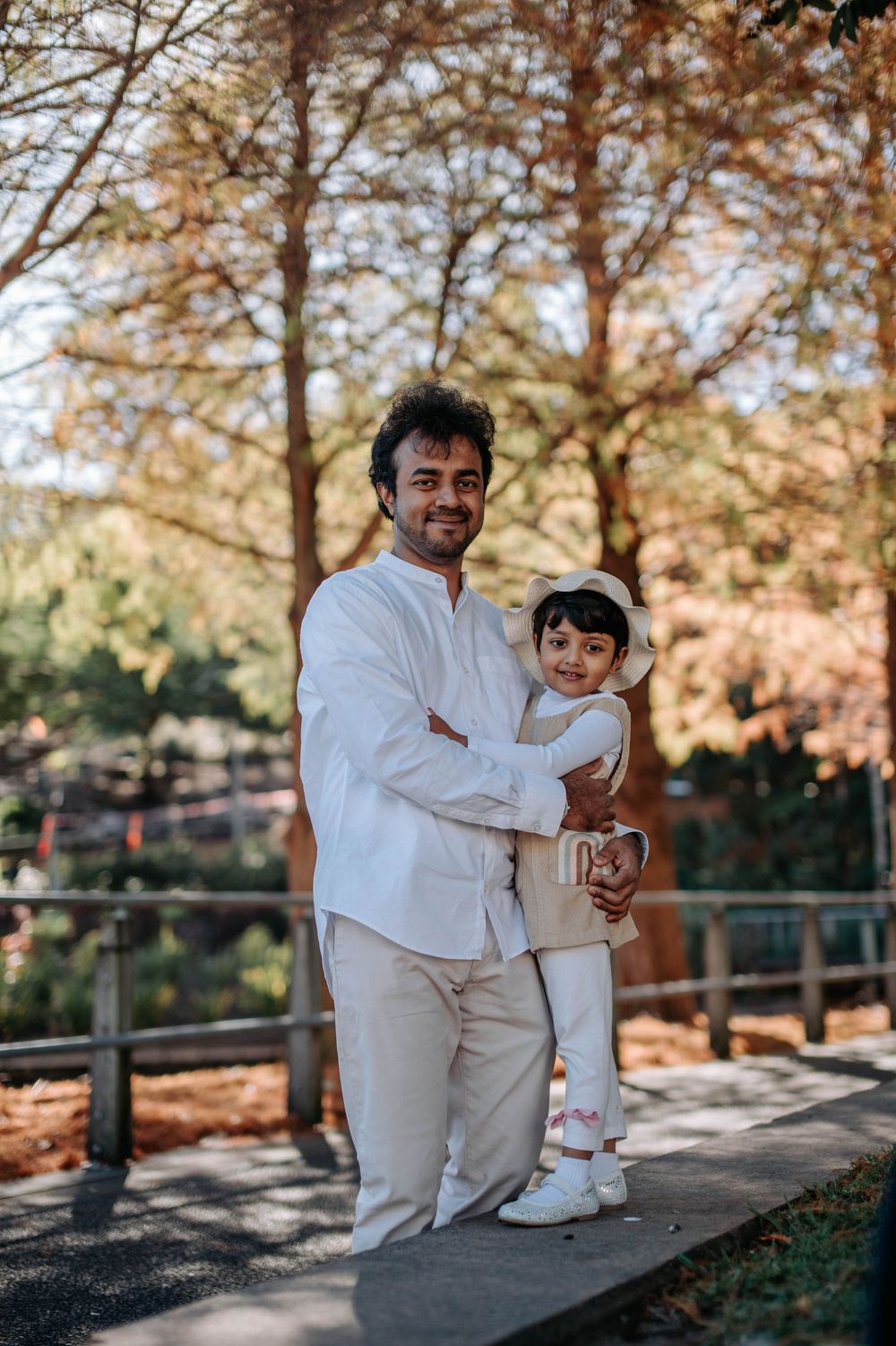 A heartwarming scene of family bonding captured in casual white outfits during a sunny autumn day at the park.