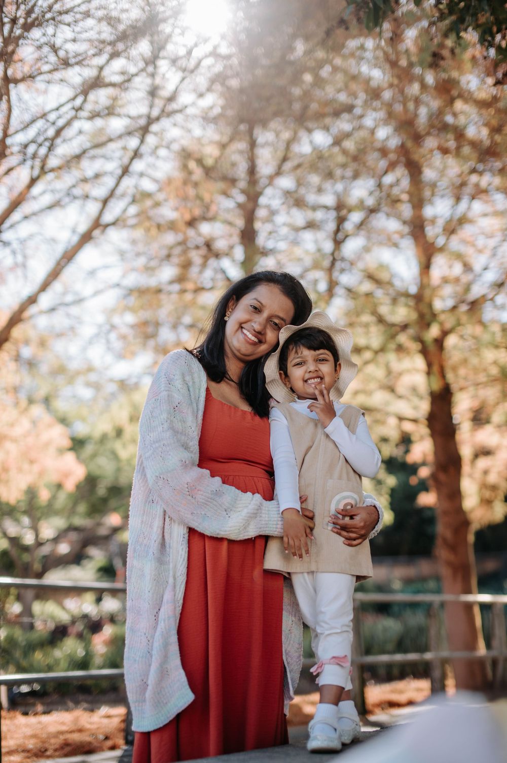 A warm autumn portrait of a mother and child standing together outdoors among fall trees.