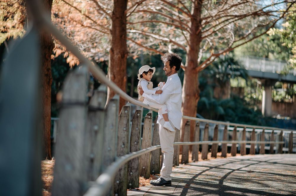 A couple in white outfits enjoys a playful moment under the autumn trees along a peaceful garden pathway.