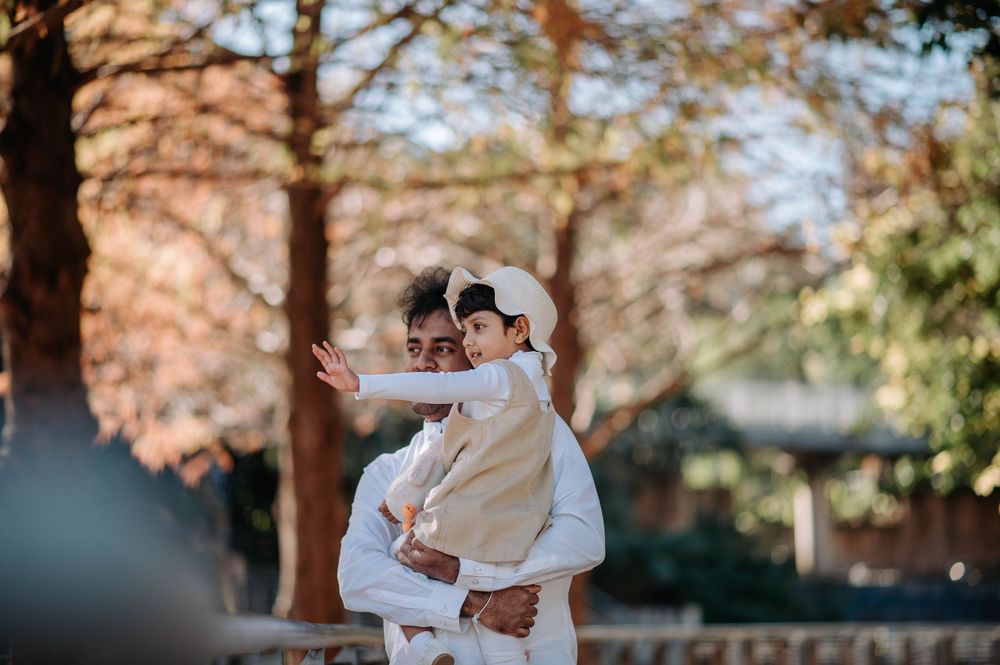 A couple dressed in all white embraces while standing among autumn trees in a park setting.