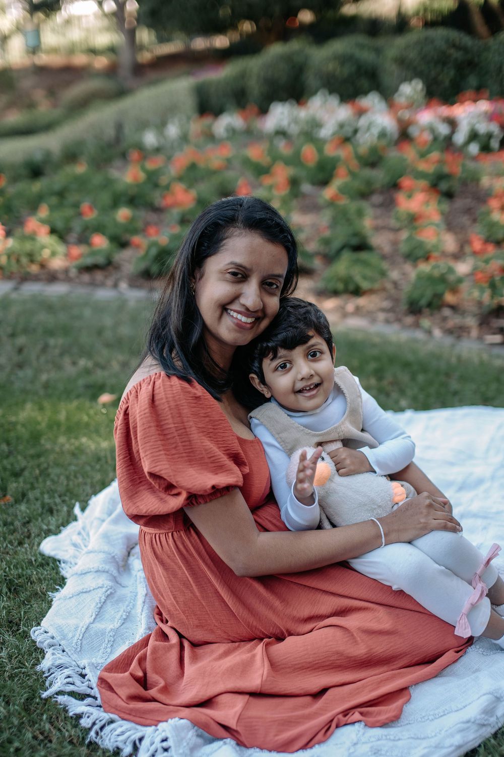 A parent and child sit together on a white blanket outdoors during a sunny autumn afternoon.