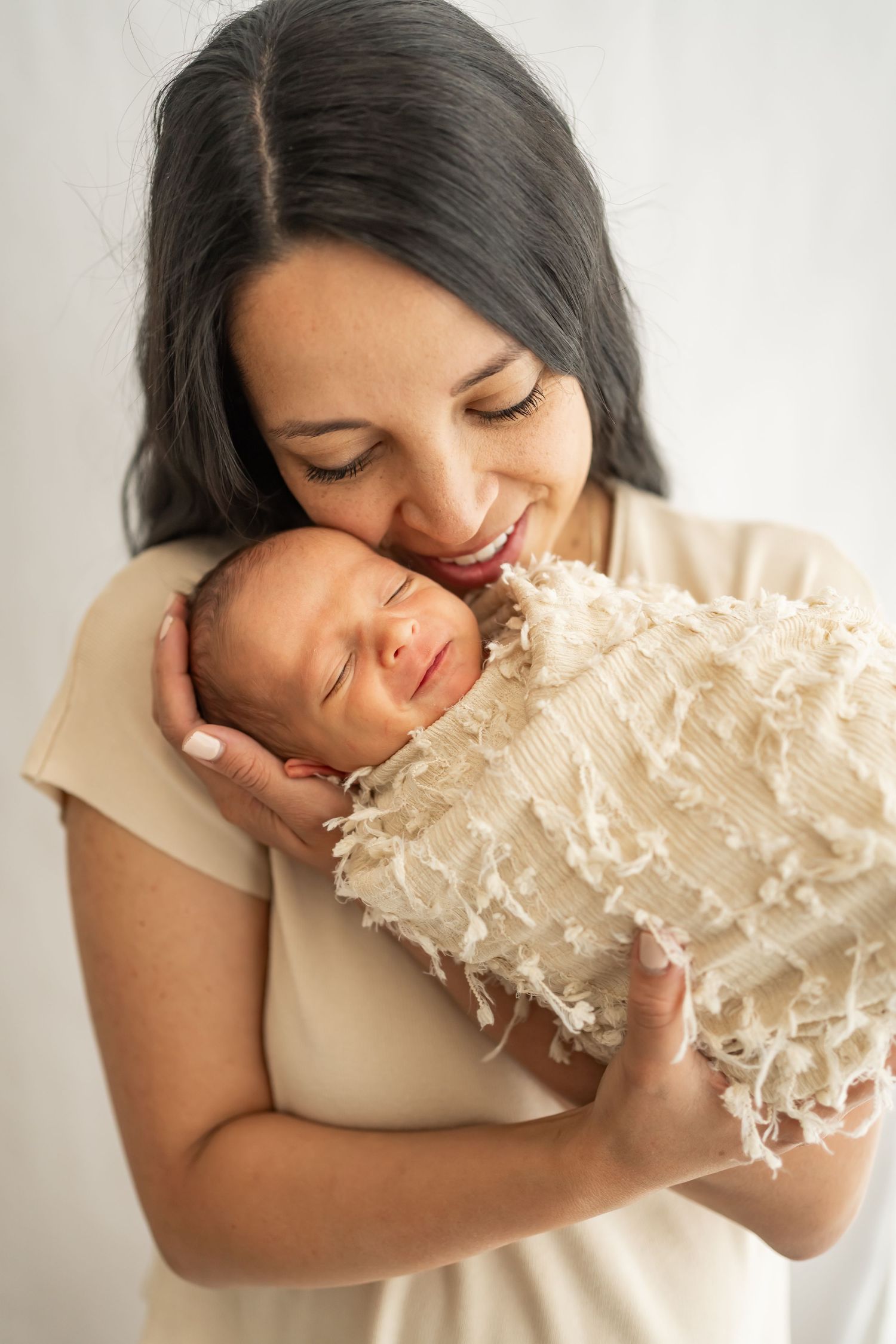 A tender moment shows a joyful embrace with a sleeping newborn baby wrapped in a textured cream-colored blanket.