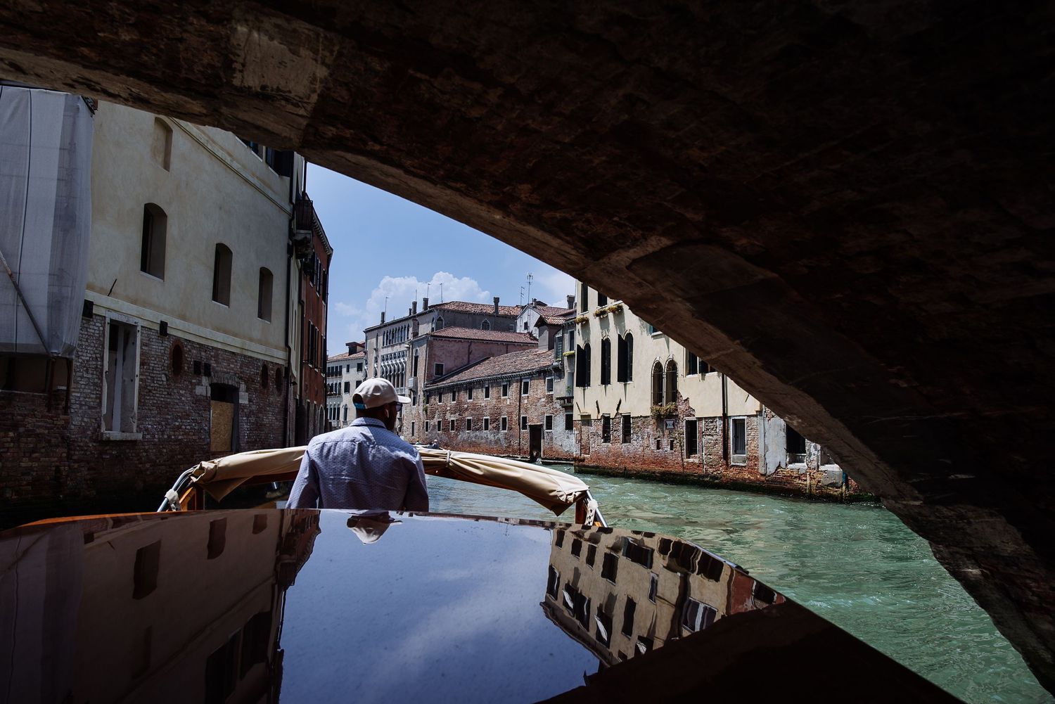 View of Venice canal through an archway with boats and buildings reflected in the water.