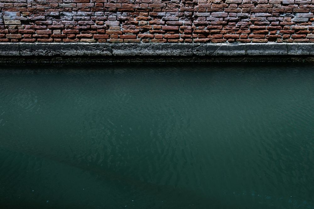 Dark green canal water meets an aged brick wall creating a minimalist urban composition.