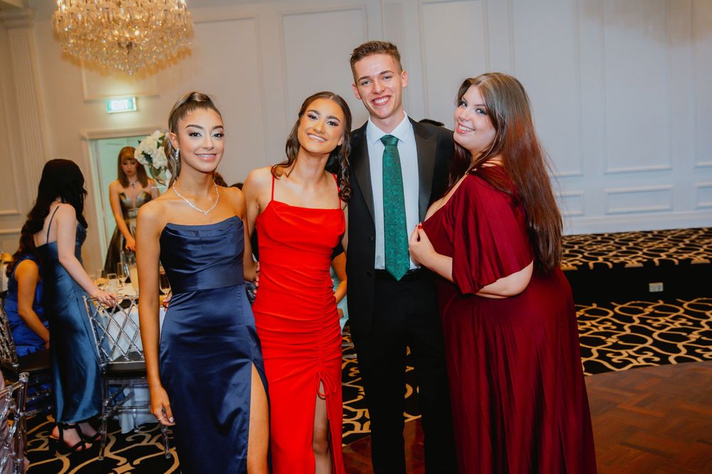 A formal event with people in elegant evening wear including navy blue, red and burgundy dresses standing in a reception hall.