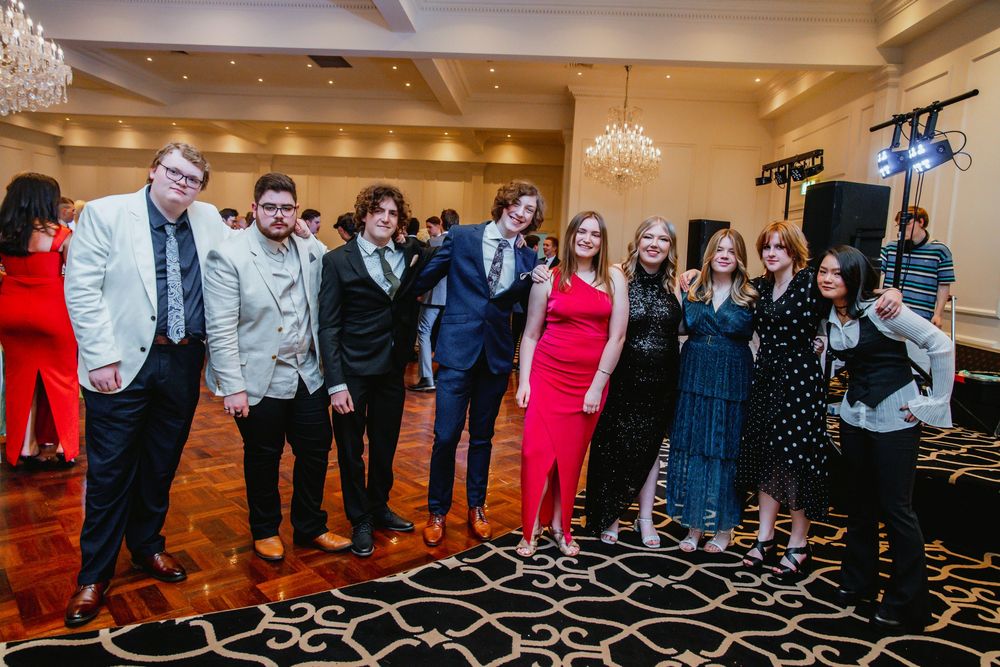 A group of wedding guests pose for photos on an elegant ballroom floor with decorative carpet patterns.